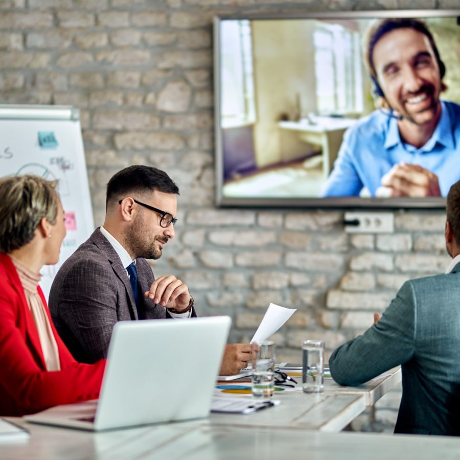 Group of entrepreneurs having a business meeting and communicating with their colleague via video call in the office.